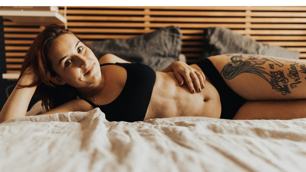 Femme en lingerie allongée sur un lit. Elle porte une brassière et une culotte noires en coton bio 