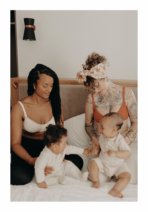 2 mamans en brassiere d'allaitement bio sur un lit en train de jouer avec avec leur bébé 