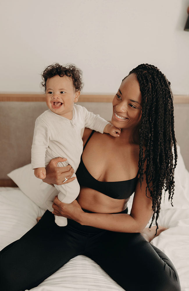 Femme accroupie, portant un soutien-gorge noir confortable en coton bio, porte un bébé dans ses bras