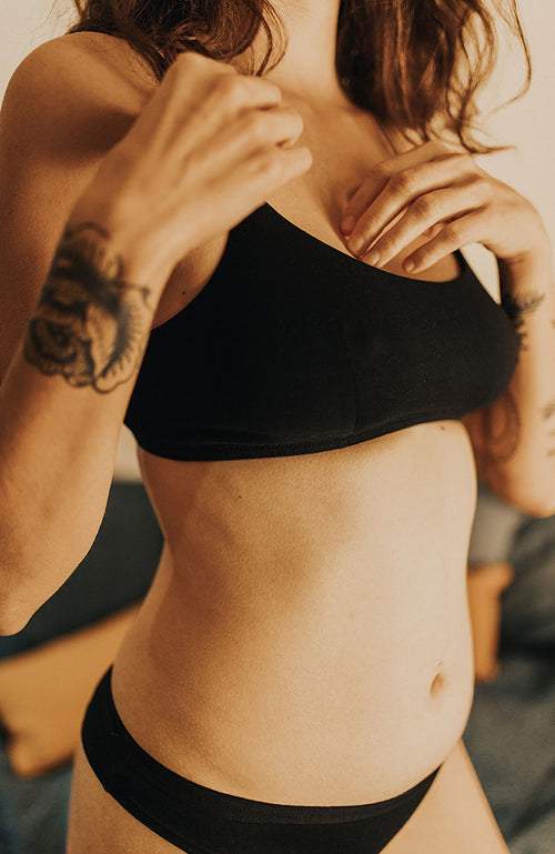 Gros plan sur une jeune femme avec tatouage, habillée avec une brassière et une culotte en coton bio noir