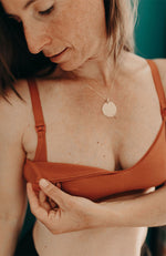 Femme portant un soutien-gorge d'allaitement terracotta, enlève le clip pour montrer le mécanisme du soutien-gorge d'allaitement