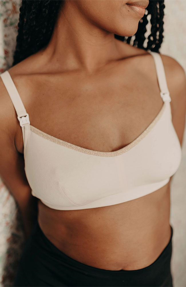 Femme debout portant un soutien-gorge d'allaitement en crème, détails dorés